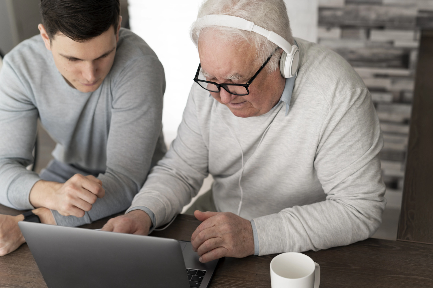 Formateur apprenant à une personne âgée à utiliser son ordinateur, illustrant la formation numérique.